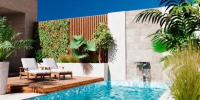 A modern outdoor pool with turquoise-colored water, two lounge chairs on a wooden deck, and green plants nearby.