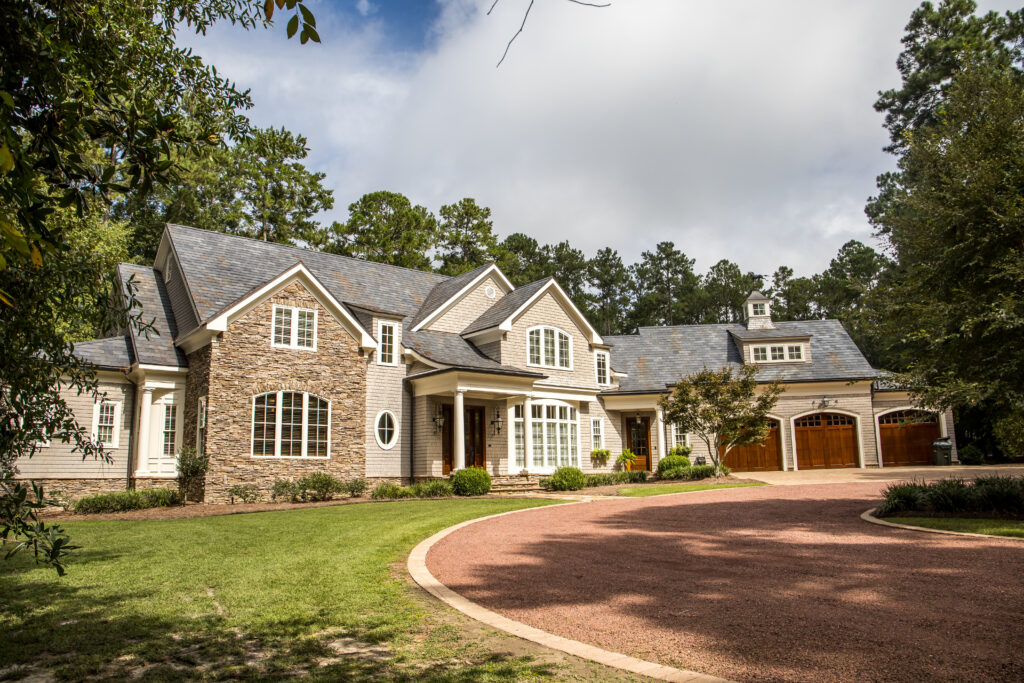 A brown gravel driveway leading up to a very large home, which features warm colors and a combination of brick and siding.