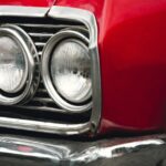 A close-up on the headlights of a classic, red car with silver detailing on the front grille and bumper.
