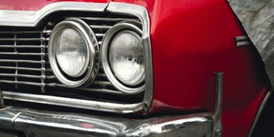 A close-up on the headlights of a classic, red car with silver detailing on the front grille and bumper.