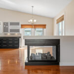 A large residential kitchen with black countertops. A small fireplace is prominently placed in the kitchen.