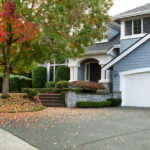 A blue house in autumn. There is a large tree next to the house with many fallen leaves surrounding it.
