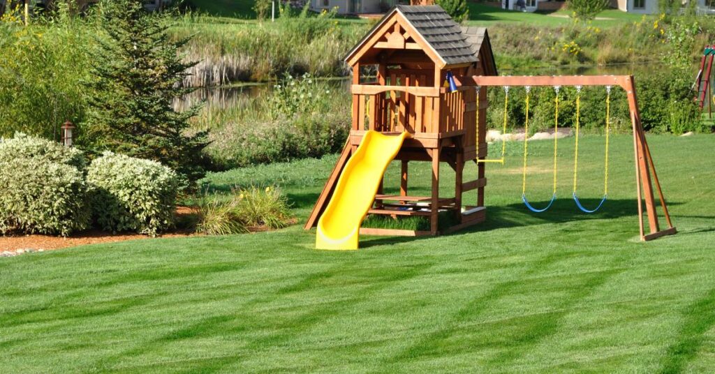 A close-up of a children's wooden playground set with a green slide and blue and yellow swing sets.