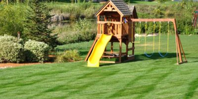 A close-up of a children's wooden playground set with a green slide and blue and yellow swing sets.