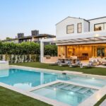 A view of a luxurious backyard with a resort-style pool, a hot tub, and an outdoor kitchen, surrounded by privacy trees.