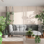 A room with a gray couch, multiple rugs, and countless plants—some hanging, others placed in pots on the floor or on tables.