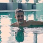 A smiling older gentleman relaxes at the edge of a luxury swimming pool.