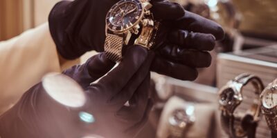 A close-up of the seller's gloved hands shows the exclusive men's watch from the new collection at the jewelry store.