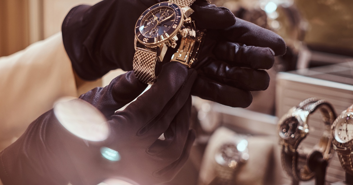 A close-up of the seller's gloved hands shows the exclusive men's watch from the new collection at the jewelry store.