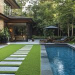 A modern, luxurious backyard with pool, patio, and lush landscaping. The house is made with brown brick.