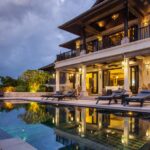 A two-story villa with open doors on the first floor and a balcony on the second. There is also a pool and patio area.