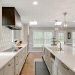 A luxury kitchen with clean, white cabinets and countertops. The backsplash is also white with a grey leaf design.
