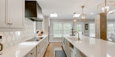 A luxury kitchen with clean, white cabinets and countertops. The backsplash is also white with a grey leaf design.