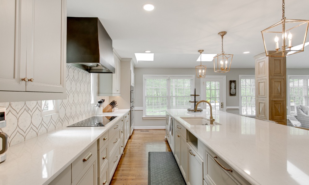 A luxury kitchen with clean, white cabinets and countertops. The backsplash is also white with a grey leaf design.