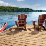 A peaceful dock with chairs set up to look over the clear water. There is also a small boat attached to the dock.