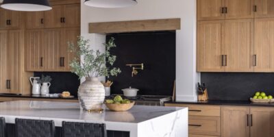 A modern kitchen with wooden cabinetry and black bar stools at the oversized marble kitchen island.