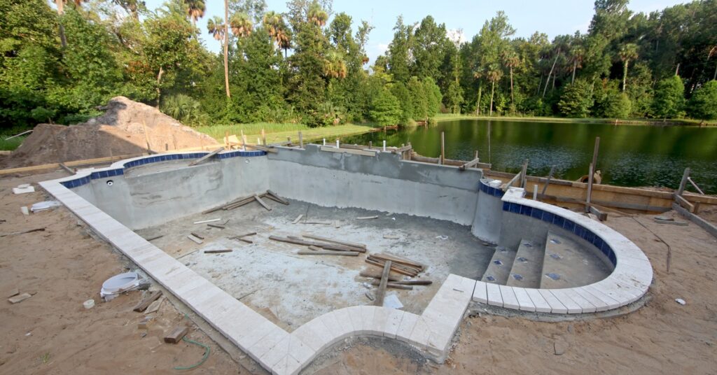 A partially constructed swimming pool with exposed concrete structure, rough edges, and unfinished surfaces.