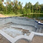 A partially constructed swimming pool with exposed concrete structure, rough edges, and unfinished surfaces.