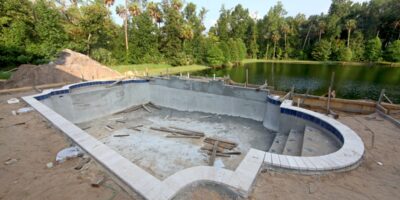 A partially constructed swimming pool with exposed concrete structure, rough edges, and unfinished surfaces.