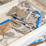 Mistakes to Avoid When Planning a Bathroom Renovation A tiled shower with the tiles on one of the walls smashed and sitting in the tub during demolition in a bathroom.