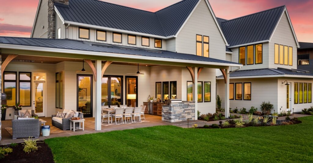The exterior of a luxury home with a large back patio and comfy seating areas. The lawn is neatly trimmed.