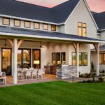 The exterior of a luxury home with a large back patio and comfy seating areas. The lawn is neatly trimmed.