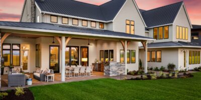 The exterior of a luxury home with a large back patio and comfy seating areas. The lawn is neatly trimmed.