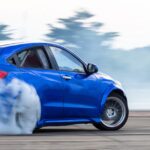 High-Performance Driving and Engine Health Tips A blue car drifts on a race track, producing lots of smoke from its rear tires. Trees can be seen in the background.