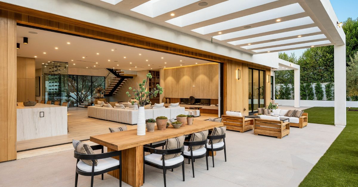 A luxury home with a large opening between the living room and outdoor living space. There is a lighted cover over the space.