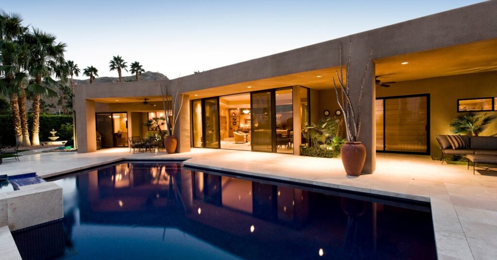 A close-up of the backyard space of a modern, minimalist-style home. There is a pool and two covered seating areas.