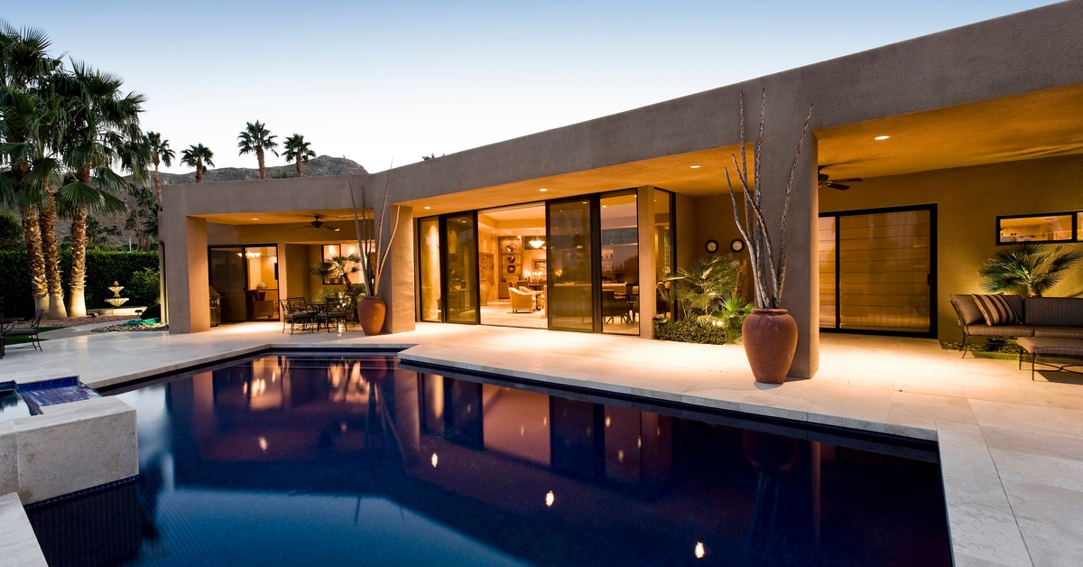 A close-up of the backyard space of a modern, minimalist-style home. There is a pool and two covered seating areas.