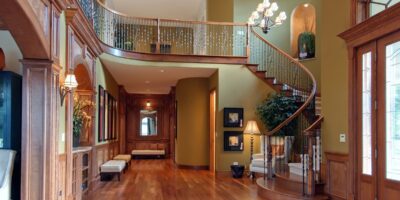 Luxury home interior with curved staircase, wood floors, chandelier lighting, and detailed trim in the entry hall.