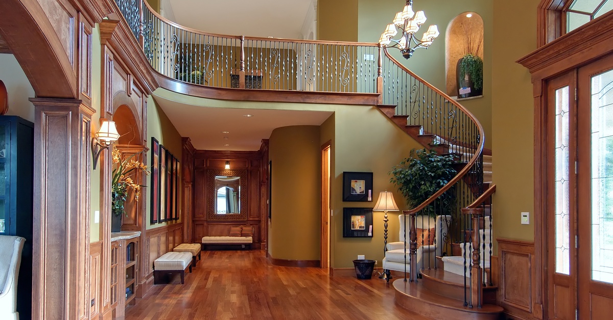 Luxury home interior with curved staircase, wood floors, chandelier lighting, and detailed trim in the entry hall.