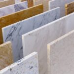 Choosing the Right Countertop Material for Your Bathroom Rows of stone countertop and tile slabs in varied white, gray, tan, and gold patterns displayed upright.