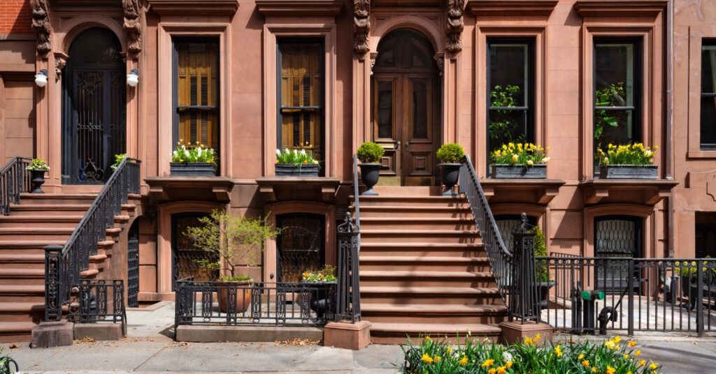 Historic brownstone facades with stone staircases, window planters, and wrought-iron fences on a residential street.