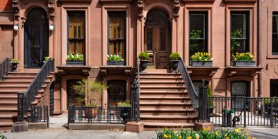 Historic brownstone facades with stone staircases, window planters, and wrought-iron fences on a residential street.