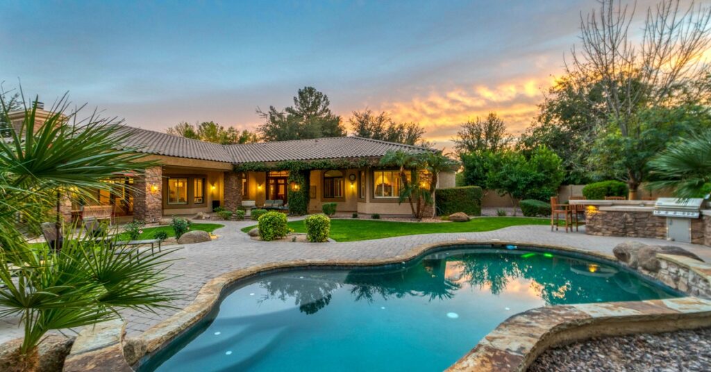 A luxury backyard with well-maintained grass, a sitting area, and a pool. Above the yard, the sun is setting.