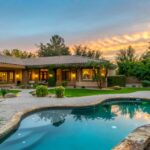 Outdoor Living Ideas That Never Go Out of Style A luxury backyard with well-maintained grass, a sitting area, and a pool. Above the yard, the sun is setting.