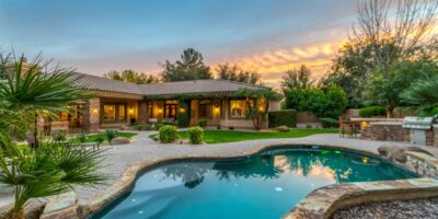 A luxury backyard with well-maintained grass, a sitting area, and a pool. Above the yard, the sun is setting.