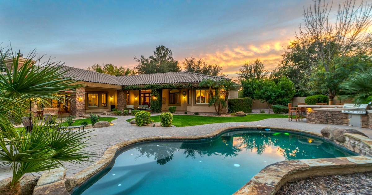 A luxury backyard with well-maintained grass, a sitting area, and a pool. Above the yard, the sun is setting.