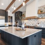 Luxury kitchen with dark cabinetry, marble island, patterned backsplash, wood floors, and exposed ceiling beams.