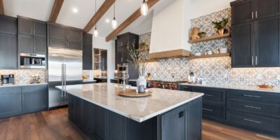 Luxury kitchen with dark cabinetry, marble island, patterned backsplash, wood floors, and exposed ceiling beams.
