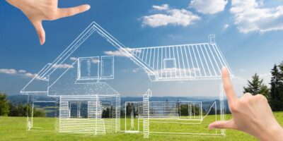 A point of view of looking at an empty grass lot with hands framing a 3D graphic of a home design sketch.