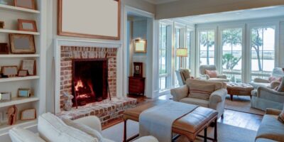 A cozy living room with white and neutral tone pieces. The fireplace has a brick surround and a white photo above it.