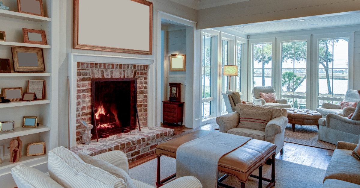 A cozy living room with white and neutral tone pieces. The fireplace has a brick surround and a white photo above it.