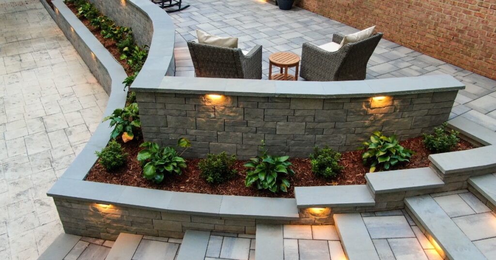 An elevated view of the backyard of a modern home with tiered stairs, outdoor furniture, and a retaining wall with plants.