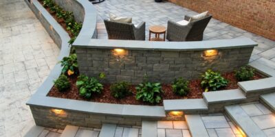 An elevated view of the backyard of a modern home with tiered stairs, outdoor furniture, and a retaining wall with plants.
